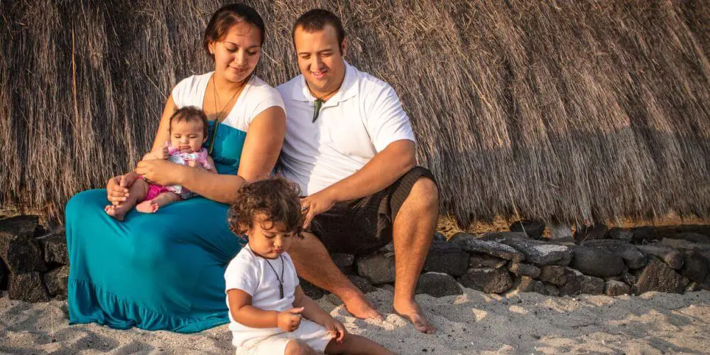 Toddler boy playes in the sand as his parents watch.