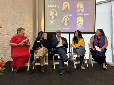 AAPIP plenary panel with five speakers seated on stage. A projection screen behind them identifies the panelists: moderator Terri Thao (Margaret A. Cargill Philanthropies), Amal Karim (ECMC Foundation/AAPIP-Twin Cities), Xay Yang (Transforming Generations), Montha Chum (Minnesota 8), and Dasharath Yata (SEWA-AIFW).